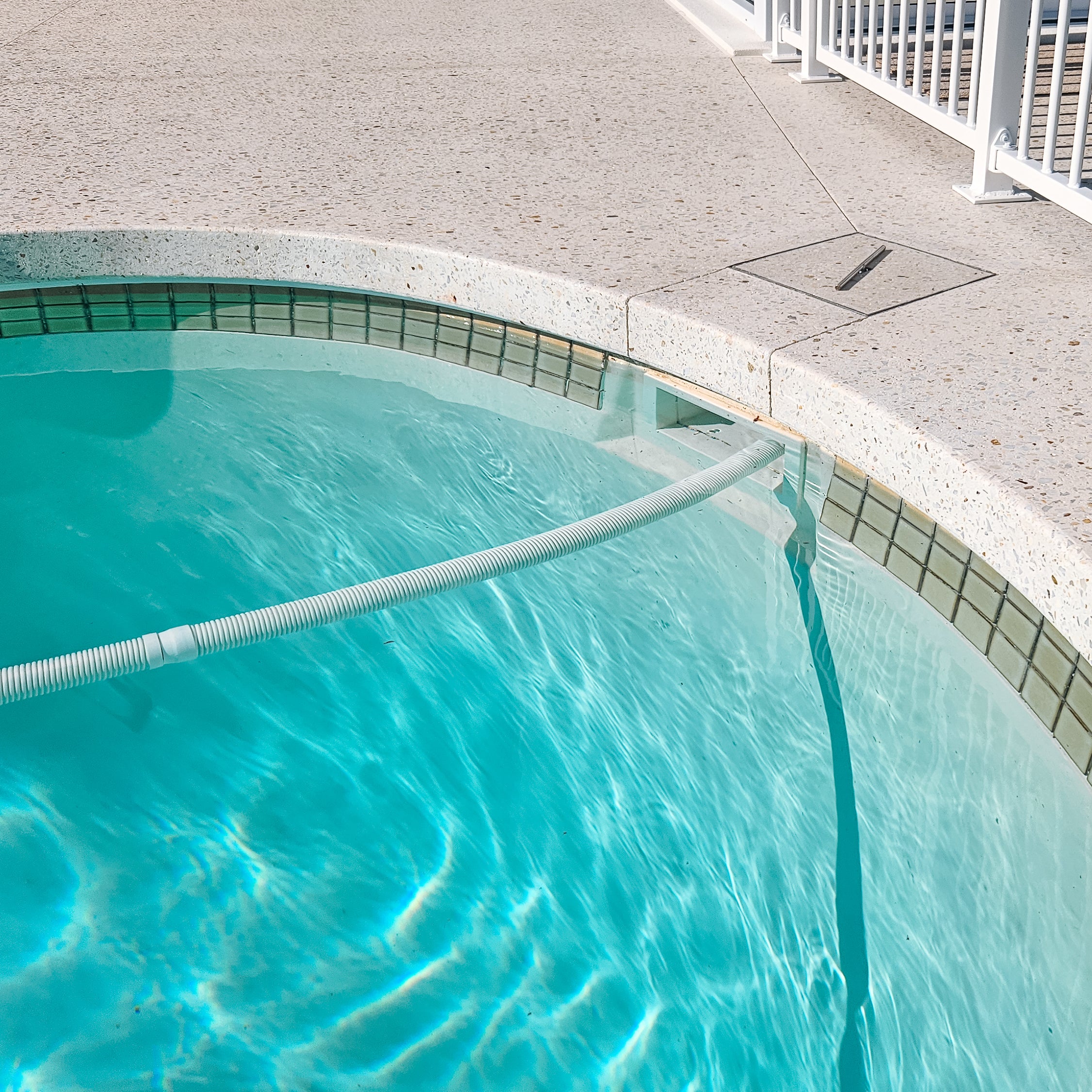 A pool skimmer box in a turquoise swimming pool with a concrete deck and white railing visible around the edge.